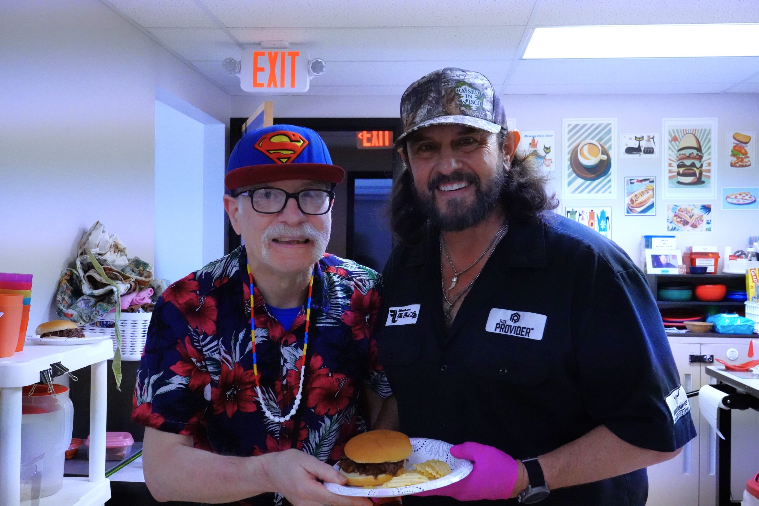 Participant and guest smile while holding a plate with a burger and chips during a luncheon.
