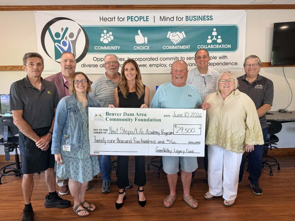 Representatives from all involved parties line up and smile while holding a big check for 29.5k.