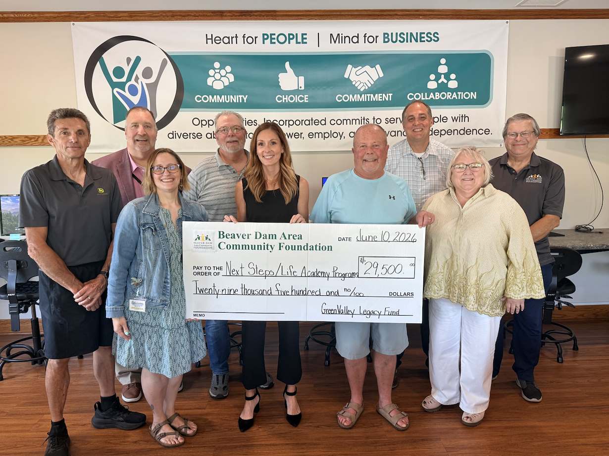 Representatives from all involved parties line up and smile while holding a big check for 29.5k.