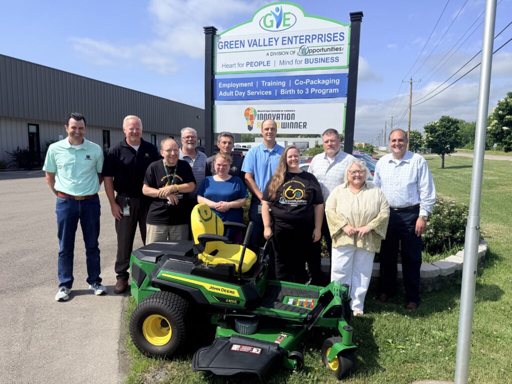 Representatives of all involved organizations line up and smile for the camera displaying the donated mower.