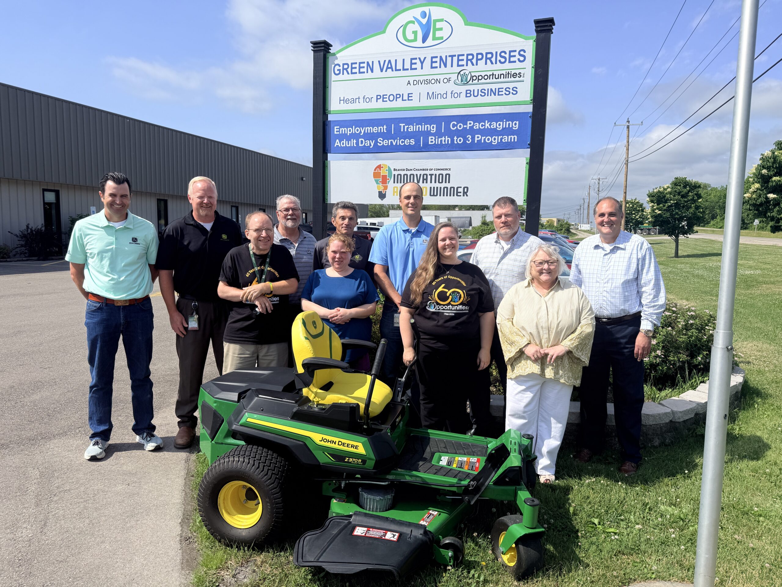 Representatives of all involved organizations line up and smile for the camera displaying the donated mower.