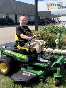 Greg Sindermann sits on a donated John Deere Z370R Electric Zero-Turn mower outside Green Valley Enterprises.