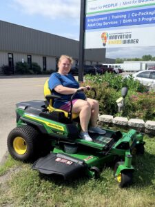Kayla DeChant sits on a donated John Deere Z370R Electric Zero-Turn mower outside Green Valley Enterprises.